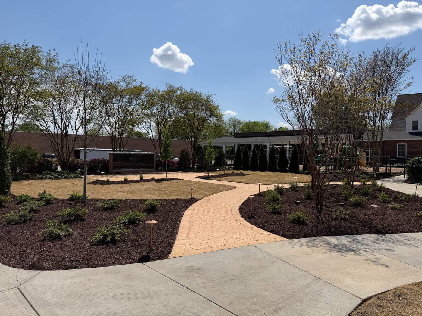 A curved paver walk through mulched beds at a commercial courtyard