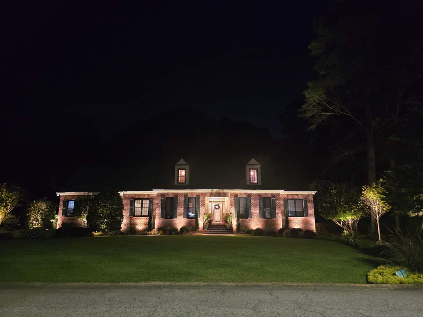 The brick home at night with landscape lighting on the facade, entry, and front lawn