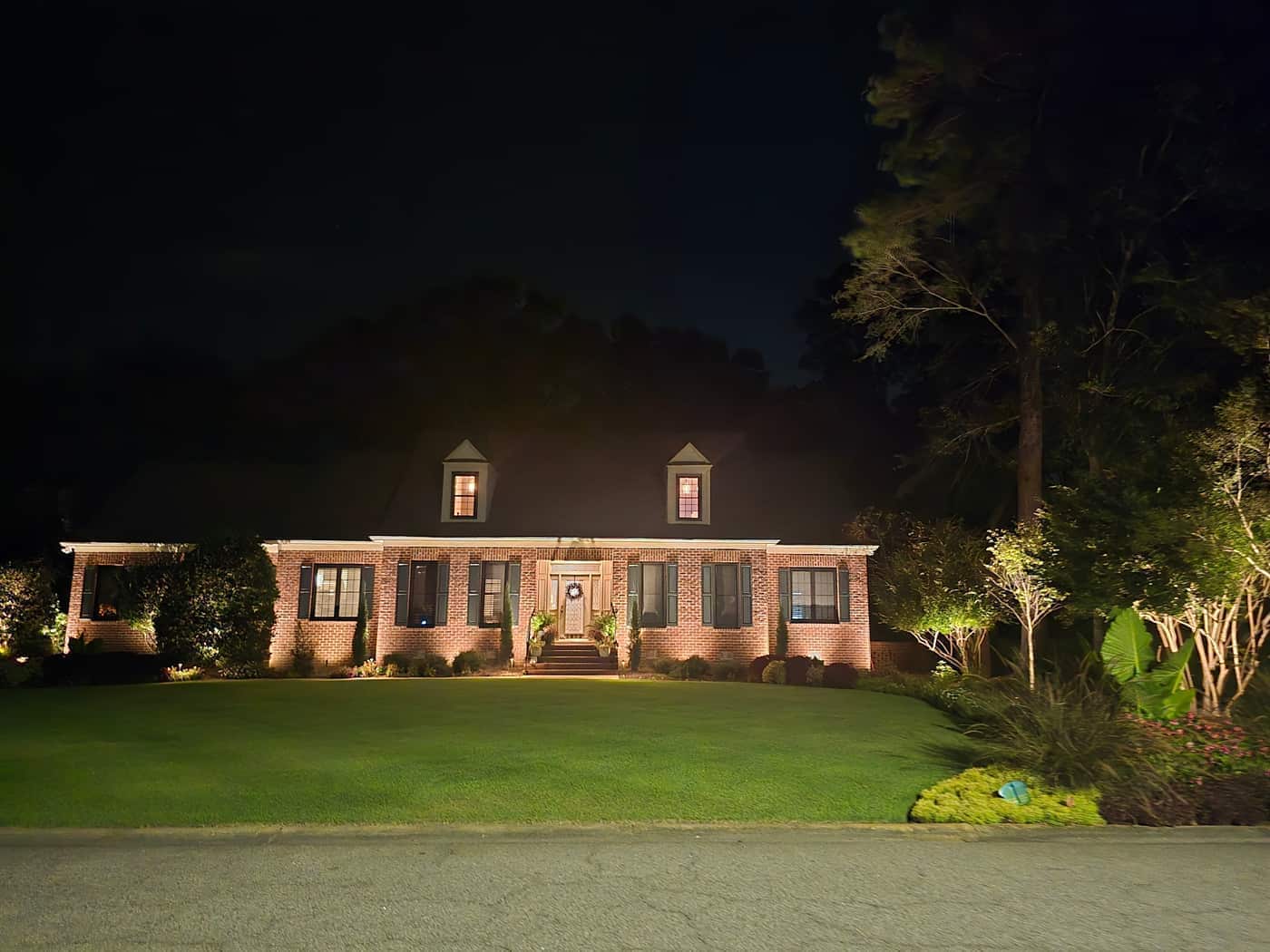 Landscape lighting across the front of the brick home, with the lawn and foundation planting lit