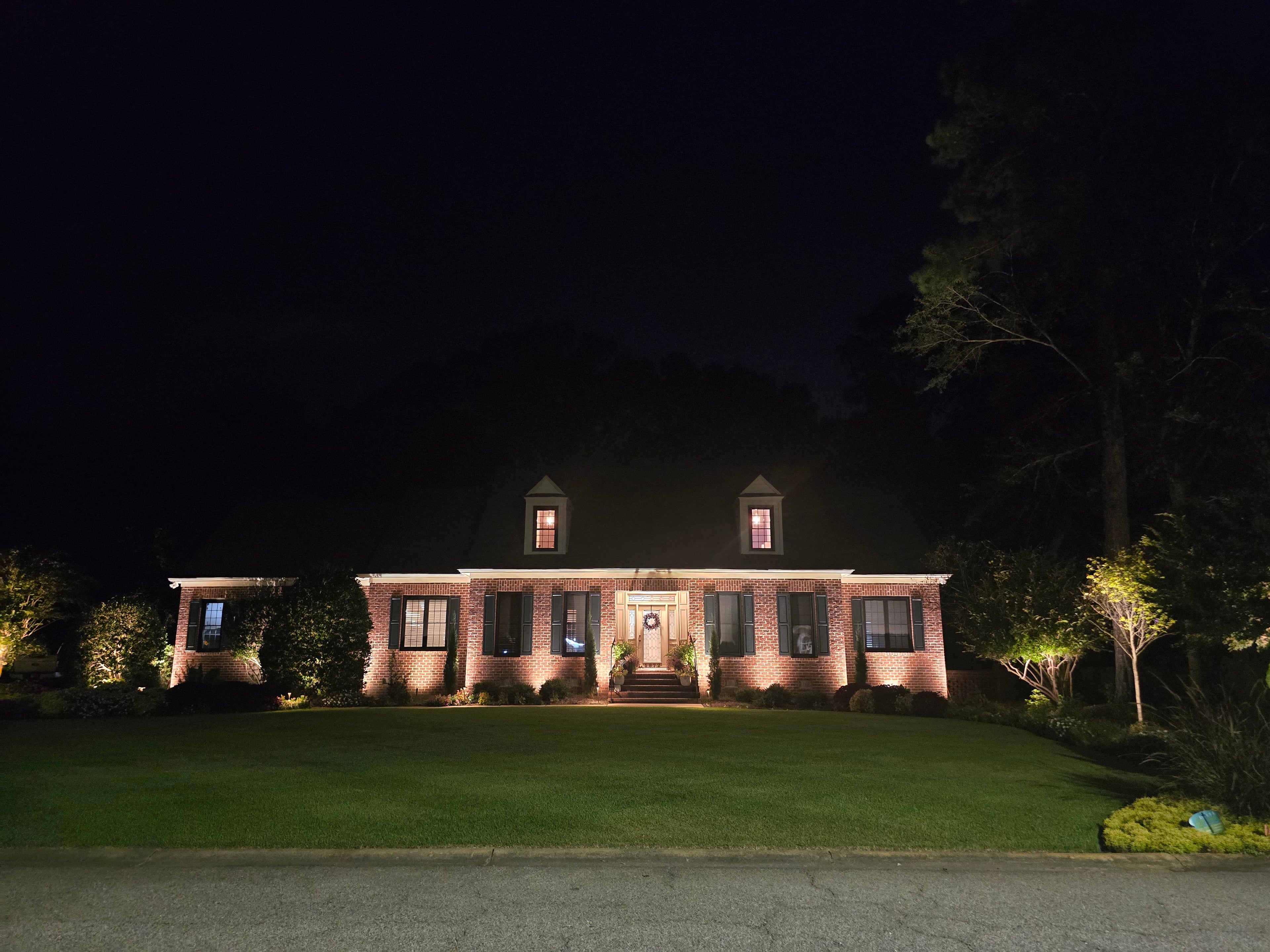 A brick home at night with landscape lighting on the facade, entry, and front lawn in Brigadoone