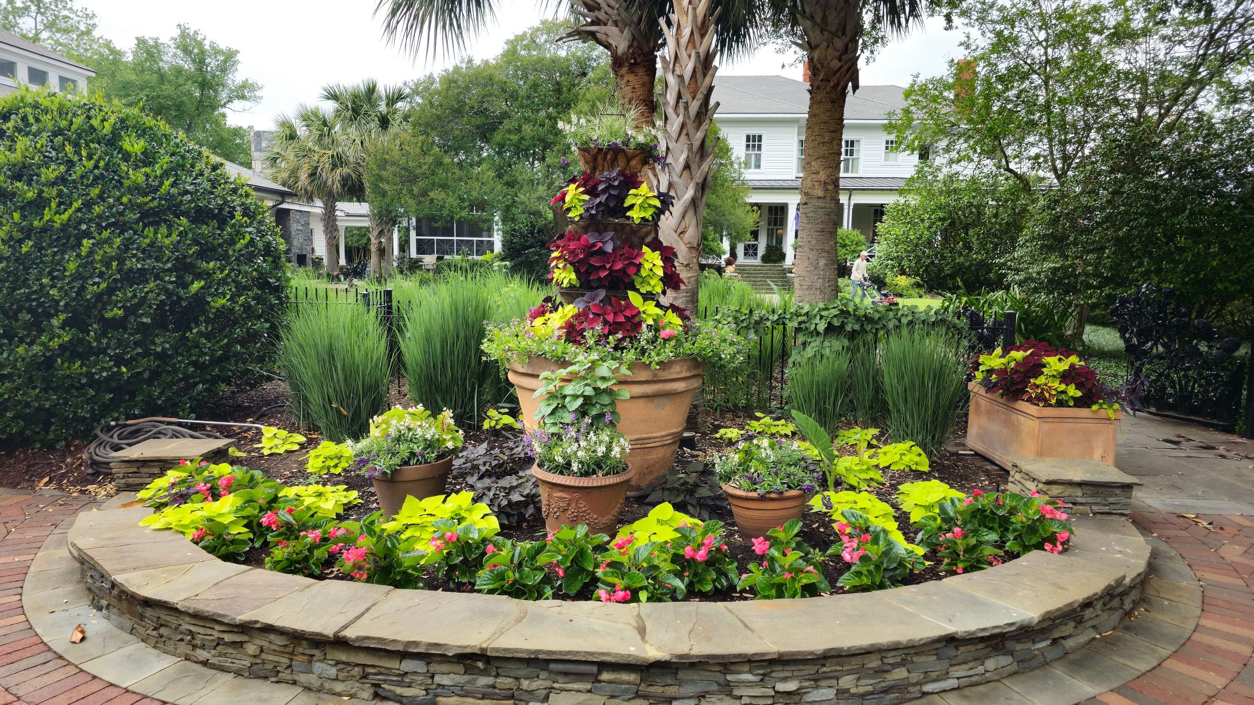 A brick courtyard with a stone planter, palms, and seasonal color