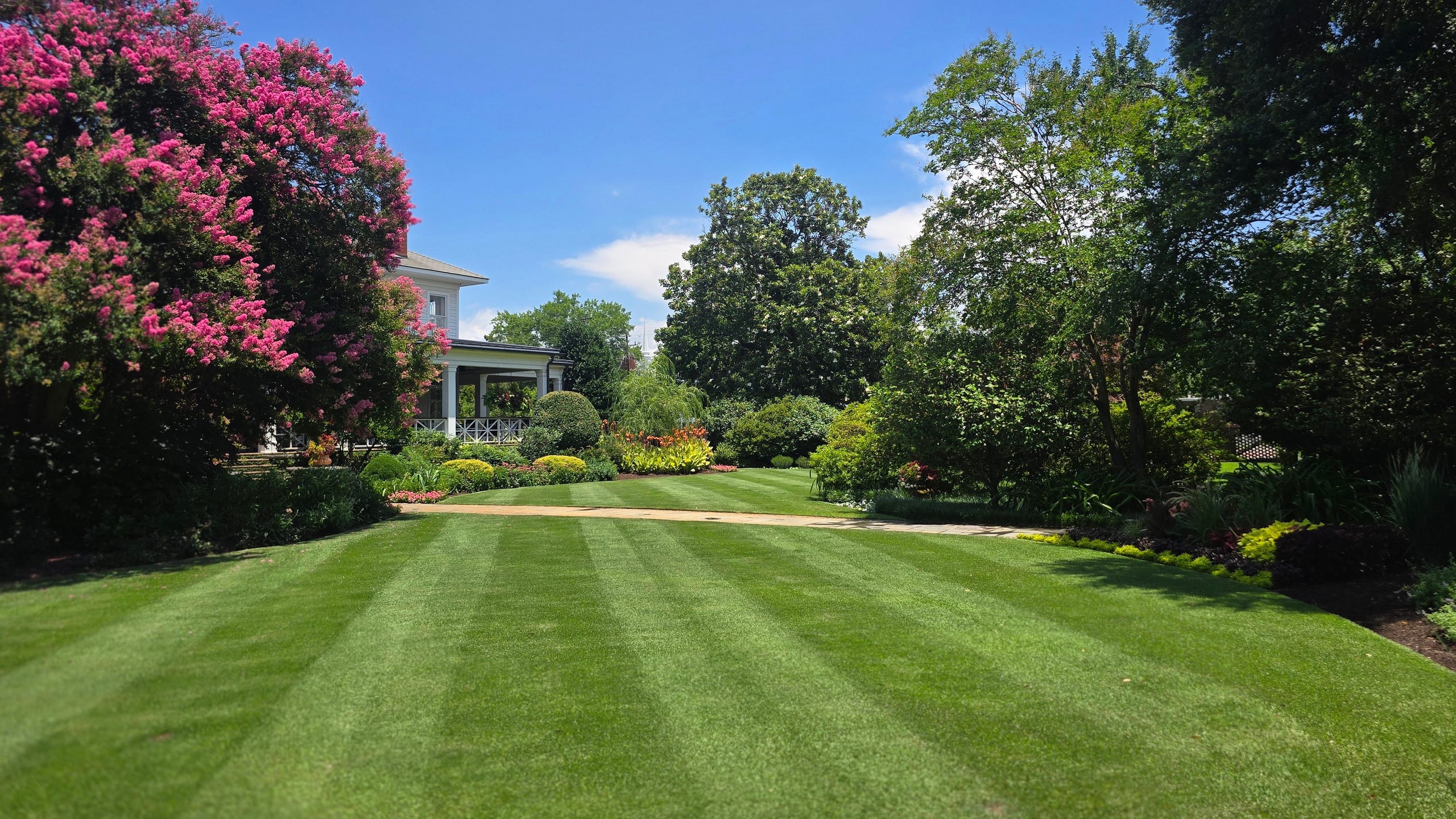 A striped lawn looking toward a white porch after professional mowing