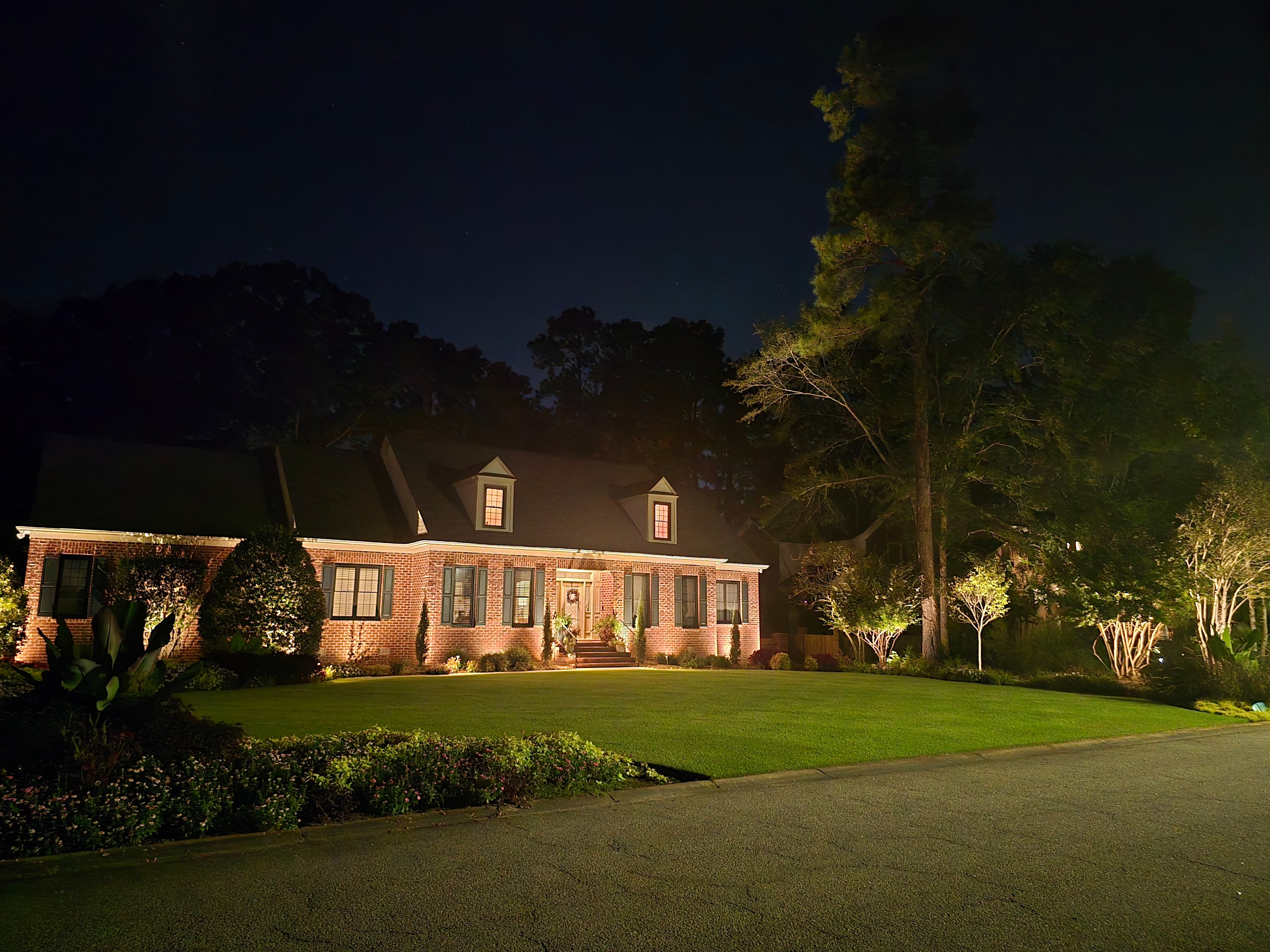 A brick home at night with landscape lighting on the lawn, entry, and trees