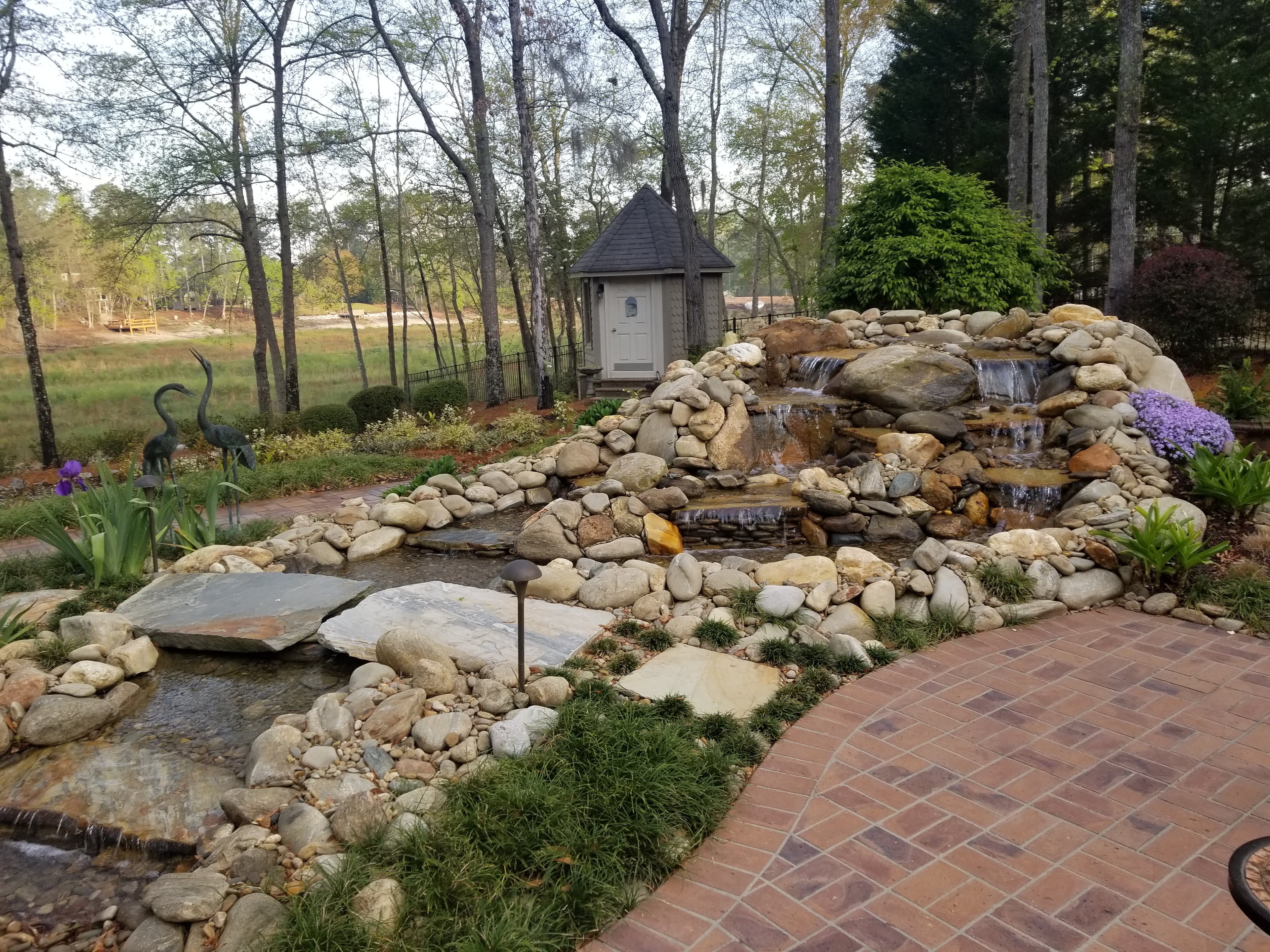 Multi-tiered backyard waterfall and stream with natural stone and plantings
